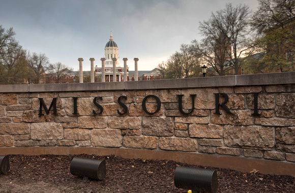 Missouri sign hung on brick wall with famous MU columns and Jesse Hall in distance